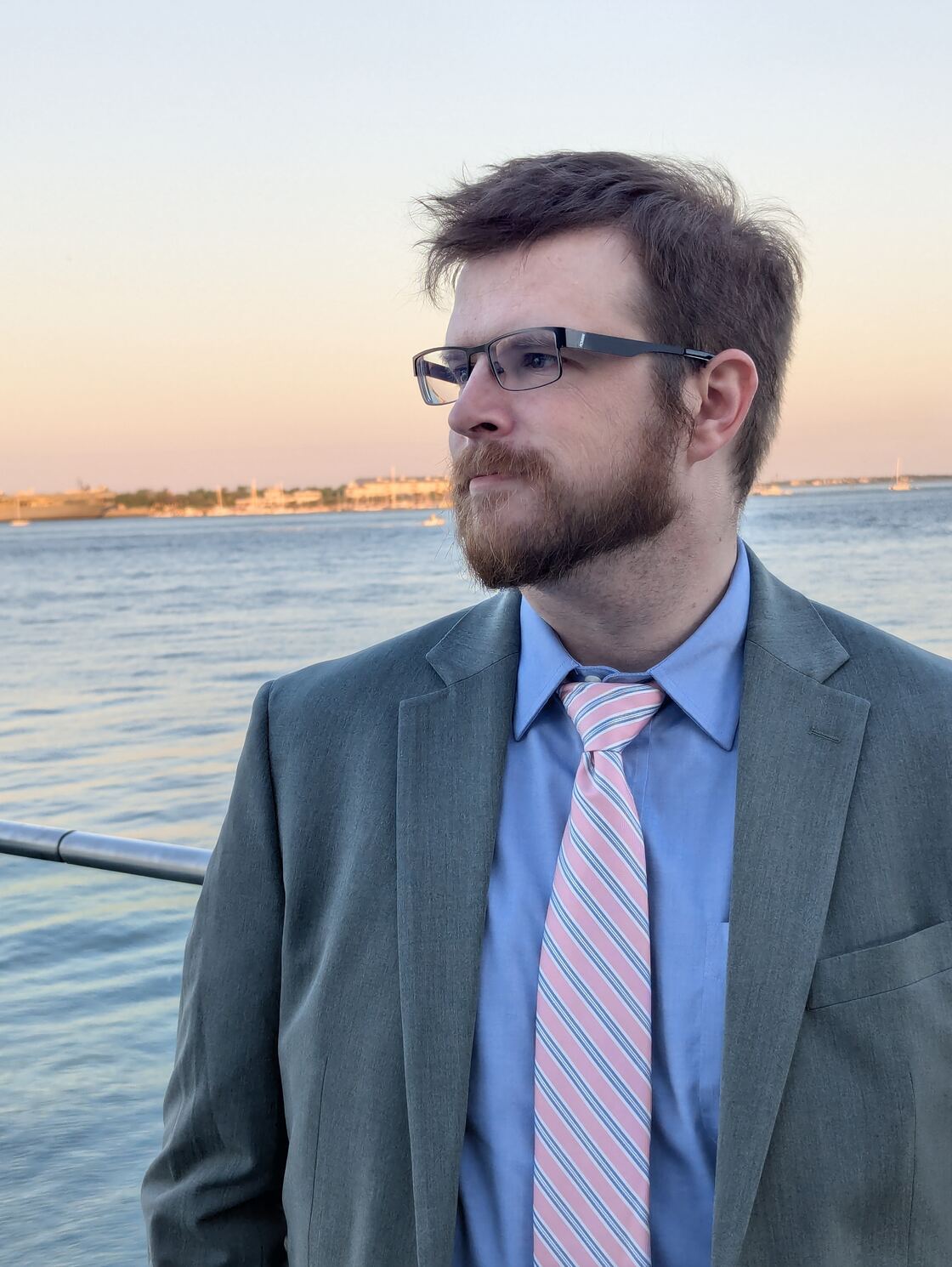 Samuel Price standing by the water at sunset in a suit and tie.