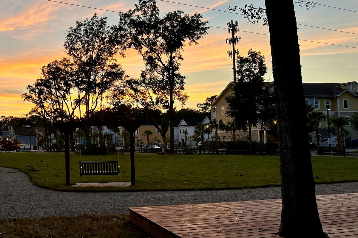 A neighborhood park in Hanahan at dusk, with a porch swing on the green and new homes behind it.