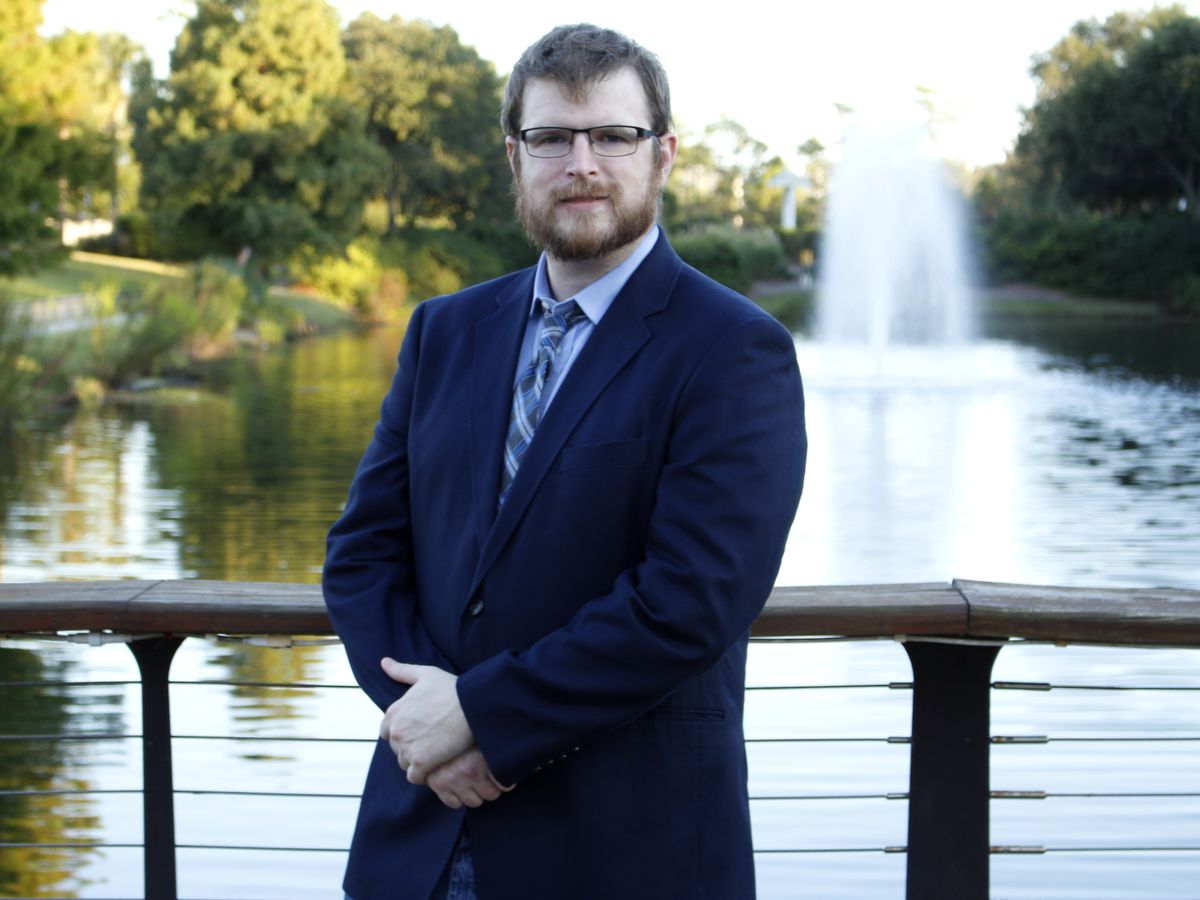 Samuel Price at a pond’s rail, a fountain behind him